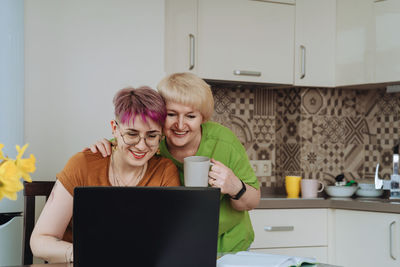 Adult mother and non-binary daughter communicate online with relatives laptop