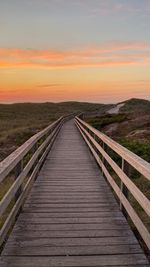 Empty wooden footbridge against sky during sunset