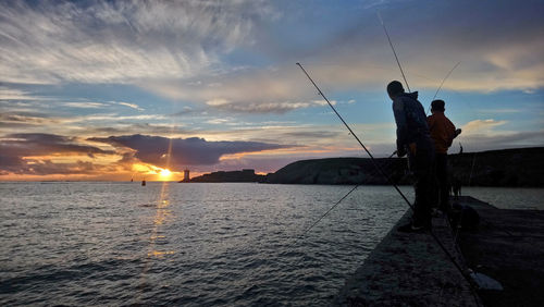 Silhouette man fishing by sea against sky during sunset
