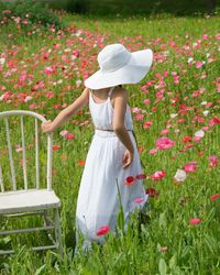 Rear view of girl in white dress with chair on poppy field