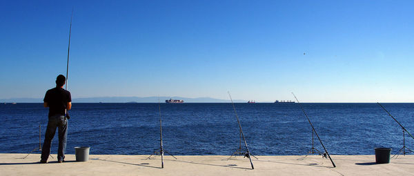 Rear view of man fishing in sea against clear sky