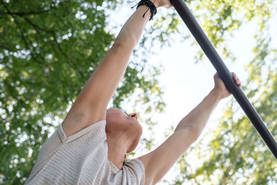 Low angle view of woman holding umbrella against trees