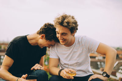 Happy friends looking at mobile phone on terrace during rooftop party