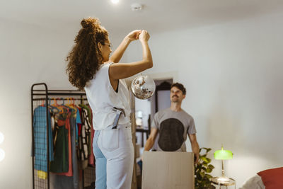 Side view of woman with hammer in back pocket holding disco ball standing at home