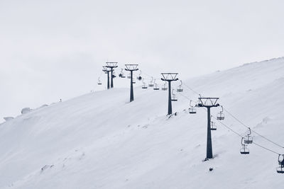 Overhead cable car on snow covered field against sky