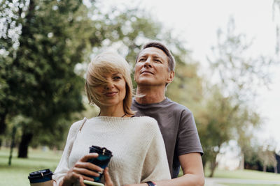 Couple embracing while holding coffee cup standing at park