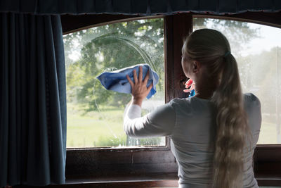 Woman cleaning window with special glass cleaner. look through soapy window