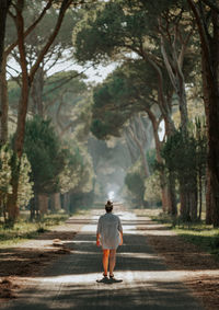 Rear view of woman walking on road along trees