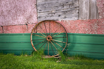 Old rusty metal wagon wheel against weathered barn board, fiber board and metal siding.