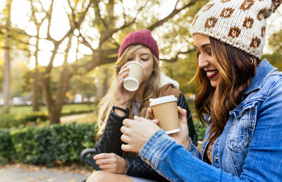 Two young women drinking coffee in a park in autumn