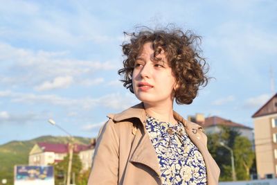 Low angle view of young woman looking away against sky