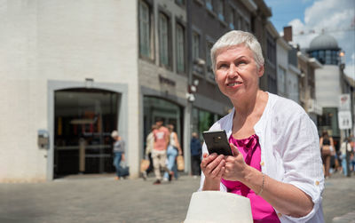 Grey haired aged caucasian woman in summer clothes chats in mobile in the city