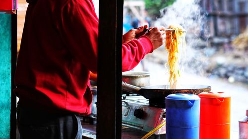 Midsection of man preparing noodles at concession stand on roadside in city