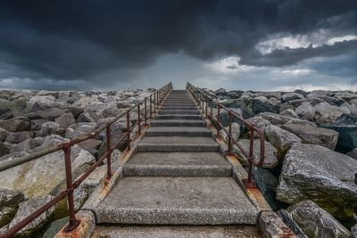 Staircase amidst rocks against cloudy sky