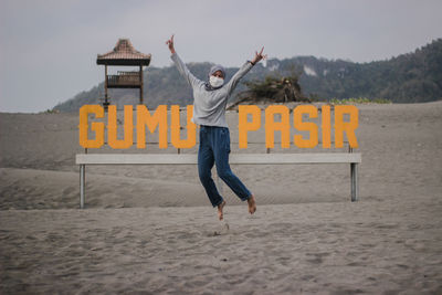 Portrait of young woman jumping by text on sand