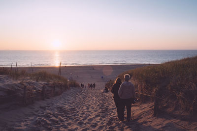 Rear view of men on beach against sky during sunset