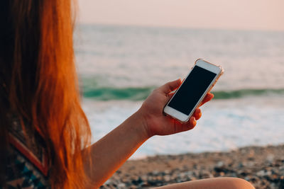 Midsection of person using mobile phone at beach