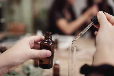 Cropped hands of female owner mixing liquid in test tube from pipette at perfume workshop