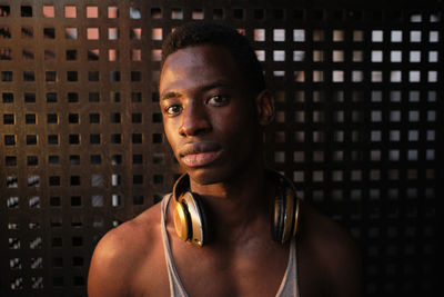 Young man with headphones around neck in front of metal wall at gym