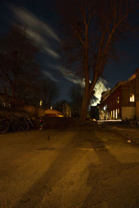 Illuminated street by buildings against sky at night