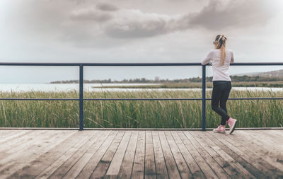 Rear view of woman leaning on railing at pier against sky