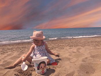 Woman sitting on beach by sea against sky