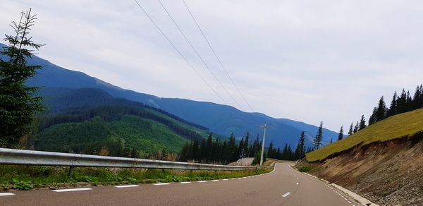 Road amidst trees and mountains against sky