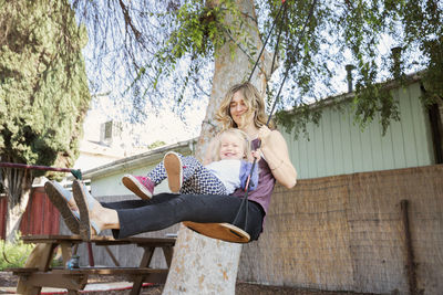 Happy mother swinging with daughter in backyard