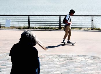 Full length of boy skateboarding on promenade in city during sunny day