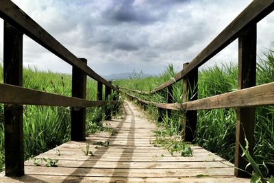 Walkway leading to pier against cloudy sky