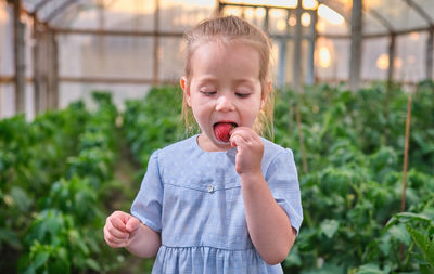 Portrait of young woman drinking water while standing against plants