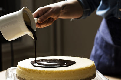 Midsection of person pouring chocolate sauce on cake