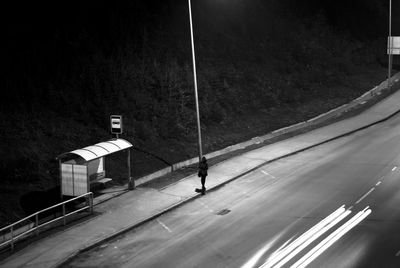 High angle view of silhouette woman walking on sidewalk by light trails at night