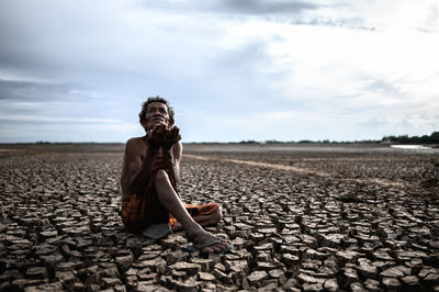 Young man sitting on land against sky