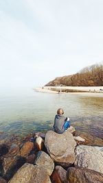 Man sitting on rock looking at sea against sky
