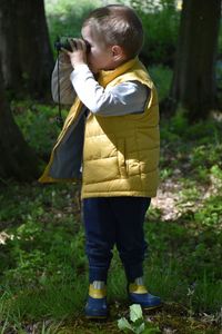 The boy looks through binoculars in the woods.