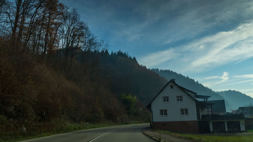 Road amidst buildings and trees against sky