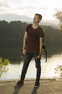 Full length of man with backpack standing by lake during sunny day