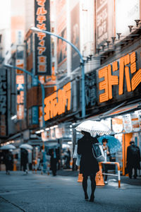 Woman with umbrella walking on road by buildings in city