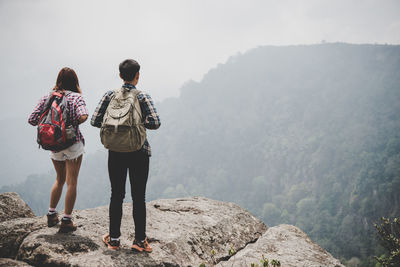 Rear view of couple standing on cliff against clear sky