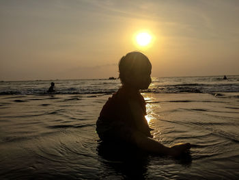 Silhouette girl sitting at beach against sky during sunset