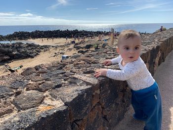 Full length of boy looking away while standing by wall against sky