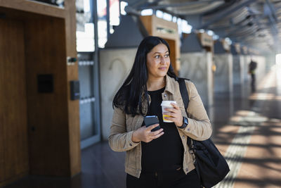 Smiling woman at train station holding disposable cup