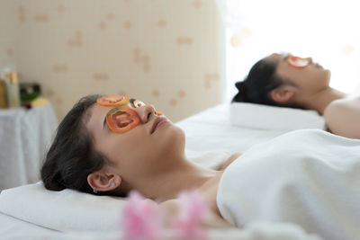 Young woman with tomato slices on eyes lying in spa