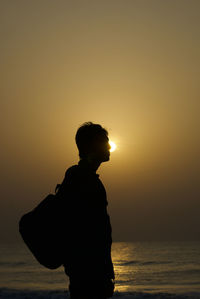 Silhouette man standing by sea against sky during sunset