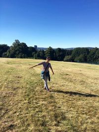 Portrait of happy young woman standing on grassy field against clear blue sky