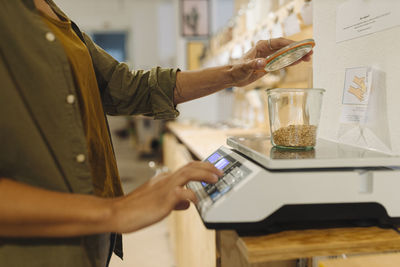 Midsection of businesswoman weighing grain jar on weight scale in cafe