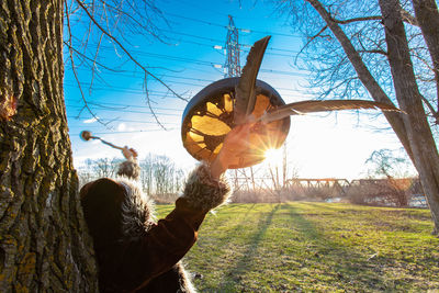 Woman holding tree trunk against sky