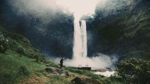 Full length of man standing by waterfall against trees
