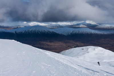 Person snowboarding on snowcapped mountain against cloudy sky